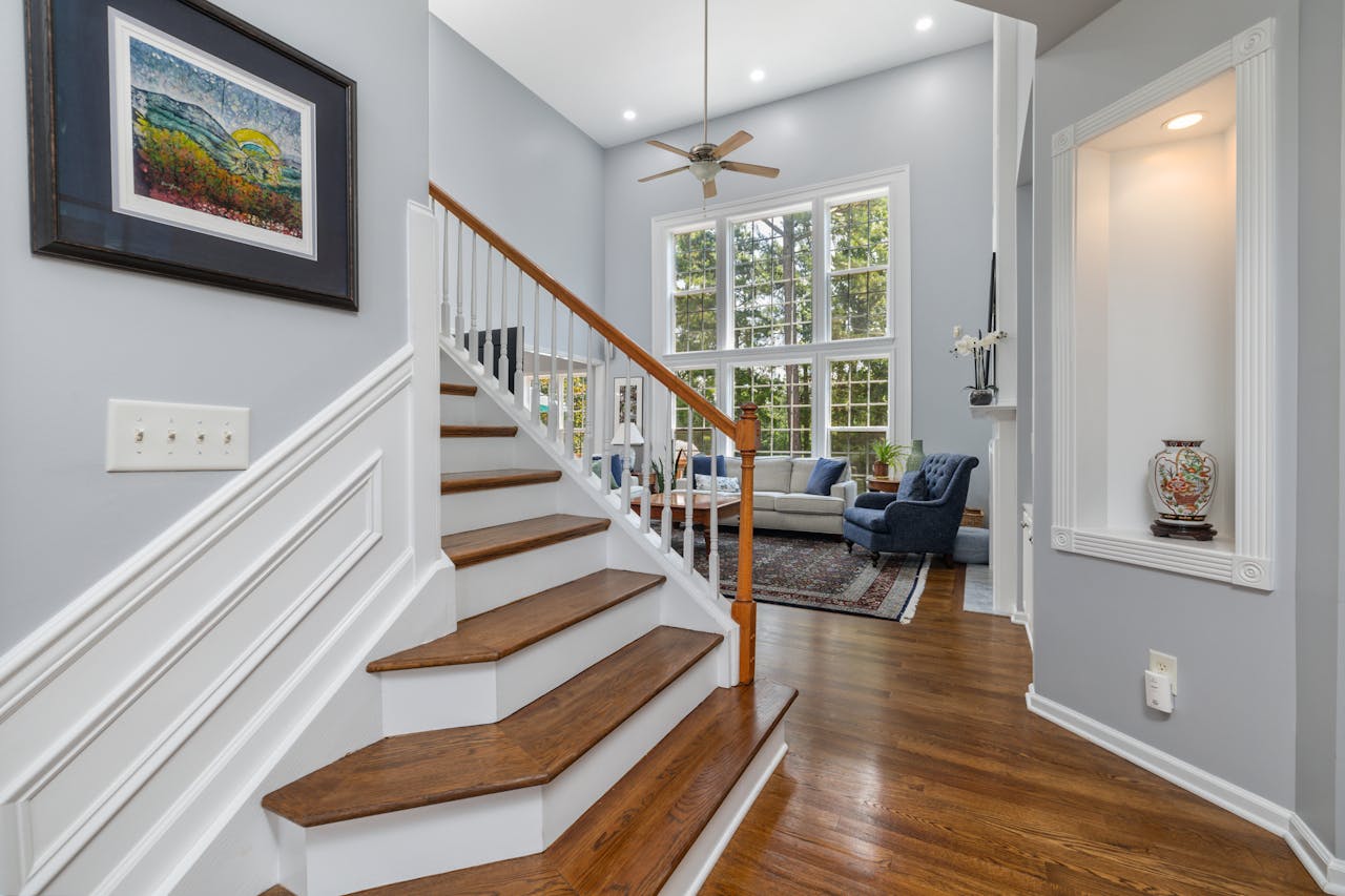 Elegant interior of a living room with staircase, large windows, and decor.