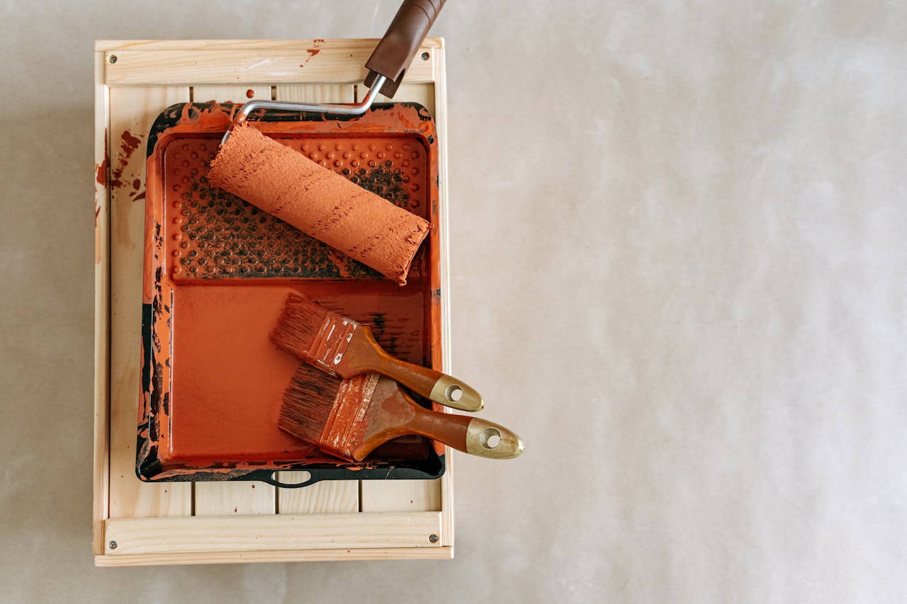 From Sun-Bleached to Stunning: The Homeowner’s Guide to Surviving South Florida’s Extreme Elements An overhead shot of paintbrushes and a roller in a tray, perfect for home renovation projects.