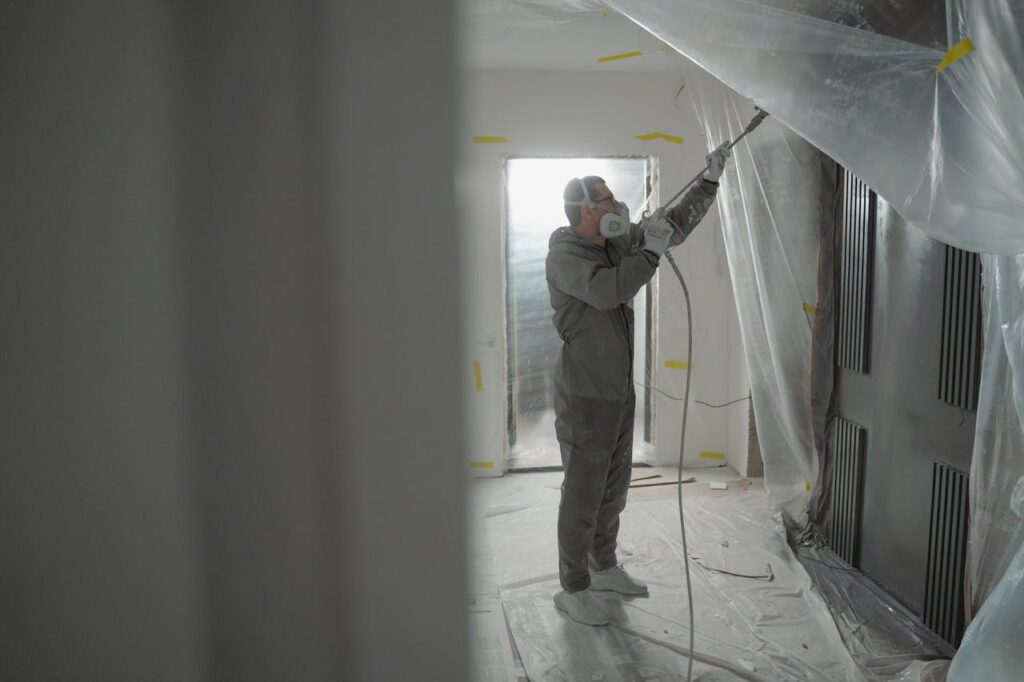 Interior Painting: How to Choose the Perfect Color Palette for Your Weston Home Man in protective gear spray painting a house's interior during renovation work.