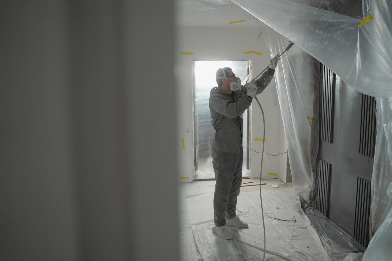 Interior Painting: How to Choose the Perfect Color Palette for Your Weston Home Man in protective gear spray painting a house's interior during renovation work.